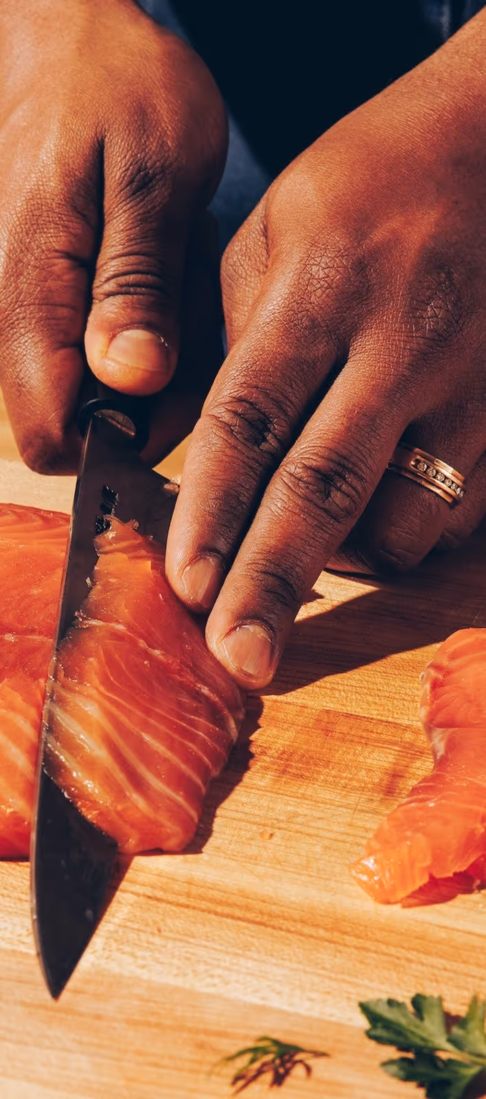 Close-up of hands slicing raw salmon on a wooden cutting board.